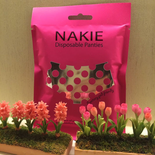 ซอง NAKIE ตั้งอยู่หลังถาดดอกไม้ประดิษฐ์ในบ้าน ของใช้ส่วนตัวที่จัดไปด้วยเมื่อน้ำท่วมต้องอพยพไปพักที่อื่น